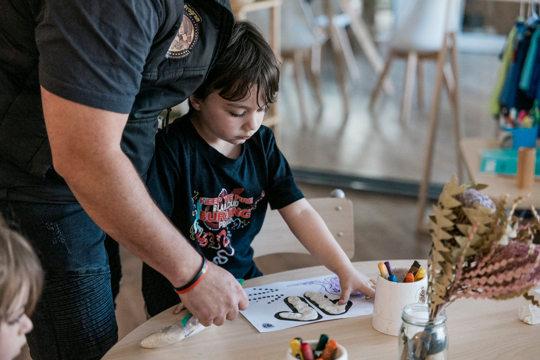 Man assisting a child to create art with playdoh and colouring paper.