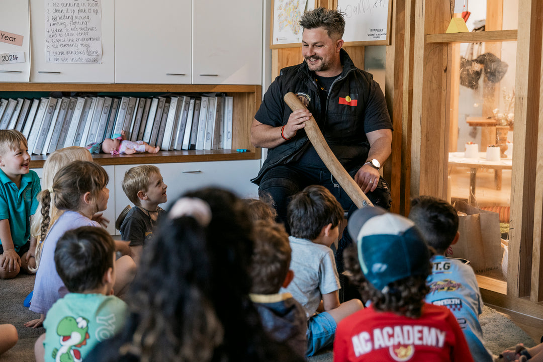 Man holding a digeridoo while talking to a class of children